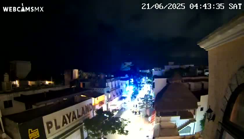 A nighttime, overhead view of a brightly lit street scene in a town or city, under a mostly clear, dark sky.