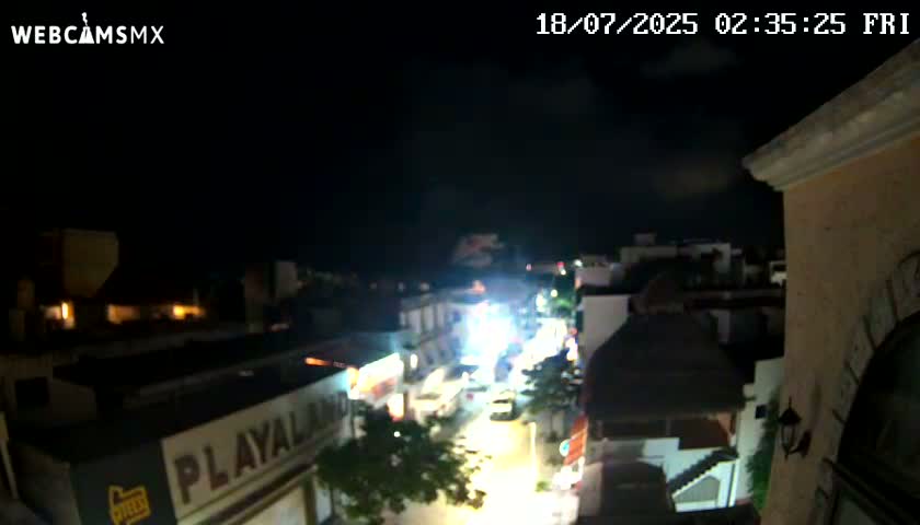 A nighttime, slightly cloudy view of a brightly lit city street below from a high vantage point.