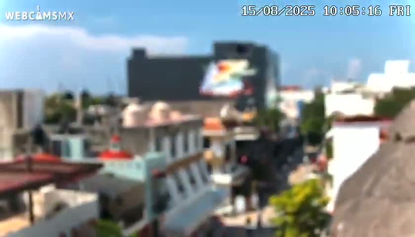 An aerial view shows a street scene with colorful buildings, lush green trees, and a clear blue sky.