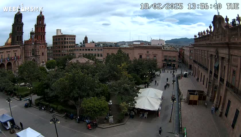 An aerial view of a city square with a cathedral, government buildings, and a park under partly cloudy skies.