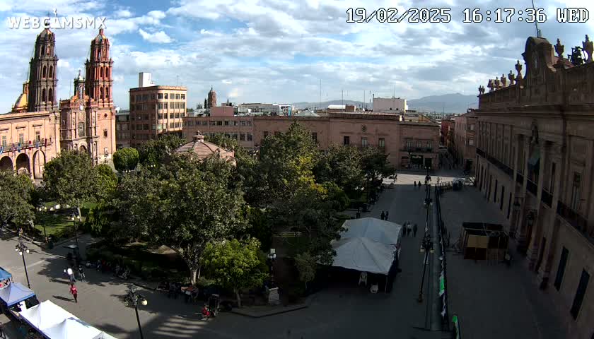 A partly sunny day overlooking a town square with a cathedral, government buildings, and numerous trees, with several tents set up in the square.