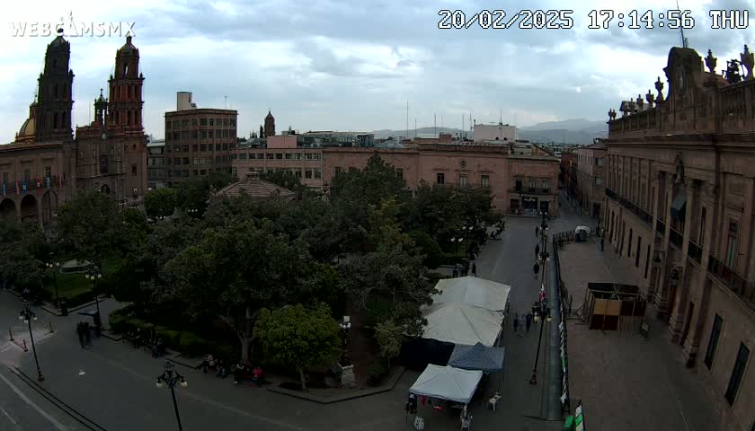 An elevated view of a town square with a cathedral and other buildings under a partly cloudy sky.