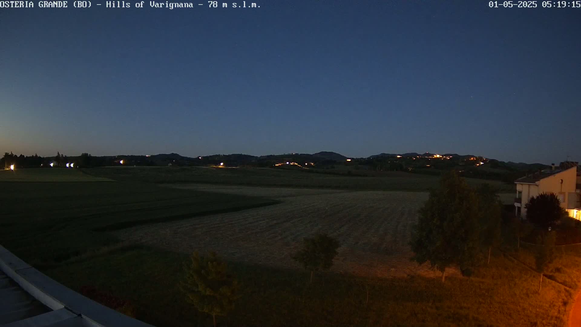 A nighttime view of a flat, dark field extending to dark hills in the distance, under a twilight sky.
