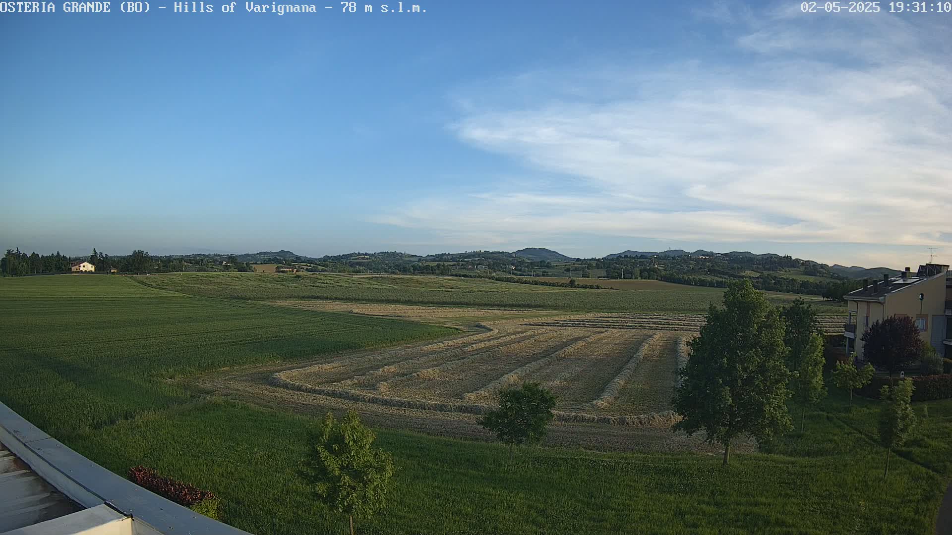 A partly cloudy sky overlooks a rural landscape of harvested fields, green pastures, and a few buildings.
