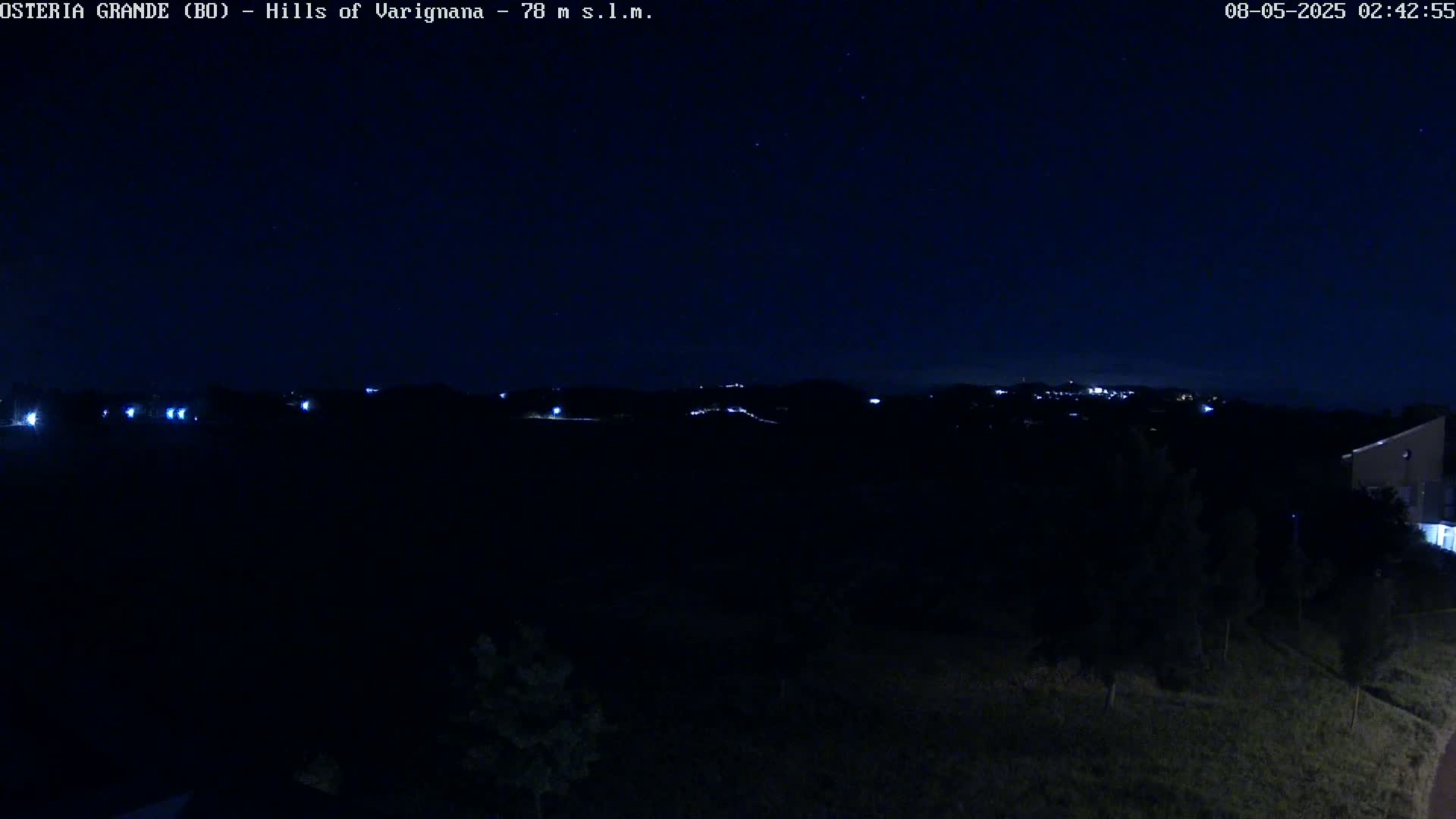 A nighttime view of dark hills and a few distant lights under a clear, star-studded sky.