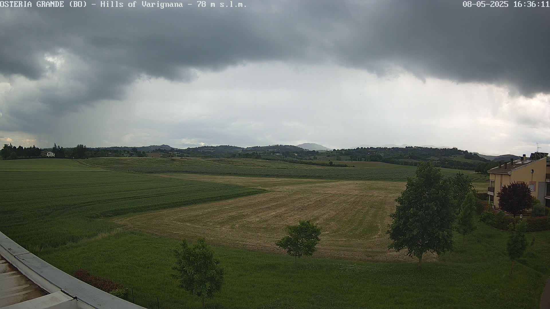 Under a mostly cloudy sky, a vast expanse of farmland stretches out to rolling hills in the distance.