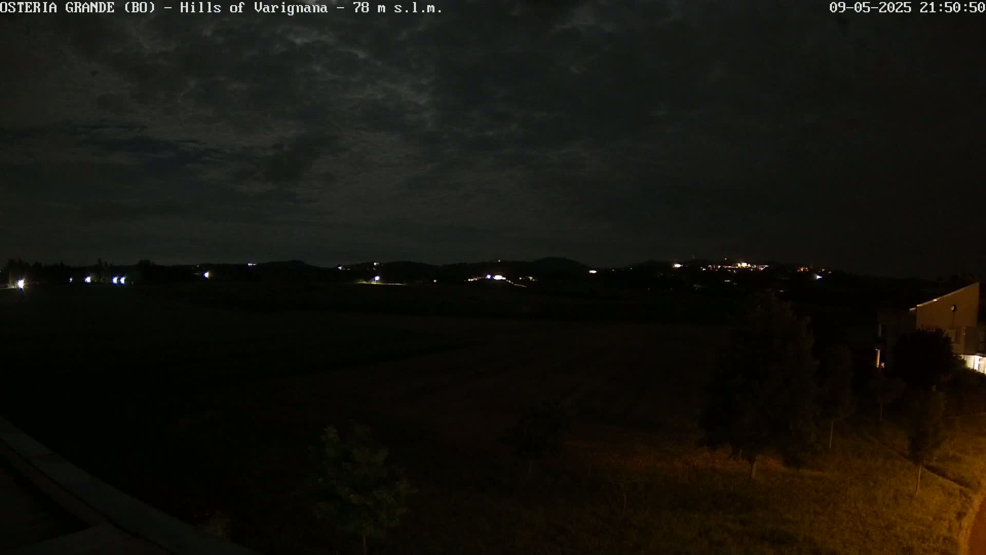 A dark, nighttime landscape shows dimly lit hills in the distance under a cloudy sky.