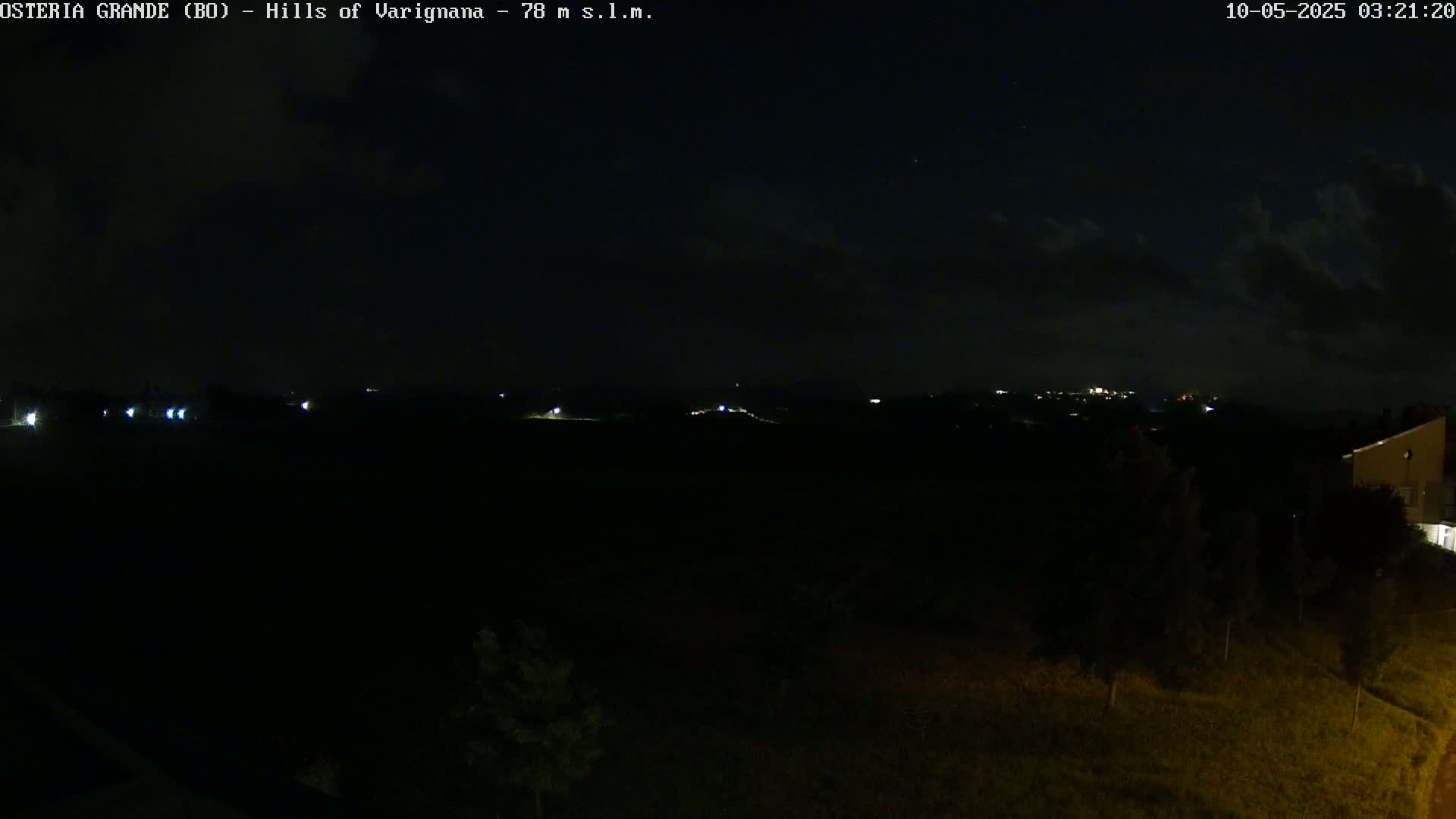 A nighttime view of dark hills and a few distant lights under a partly cloudy sky.