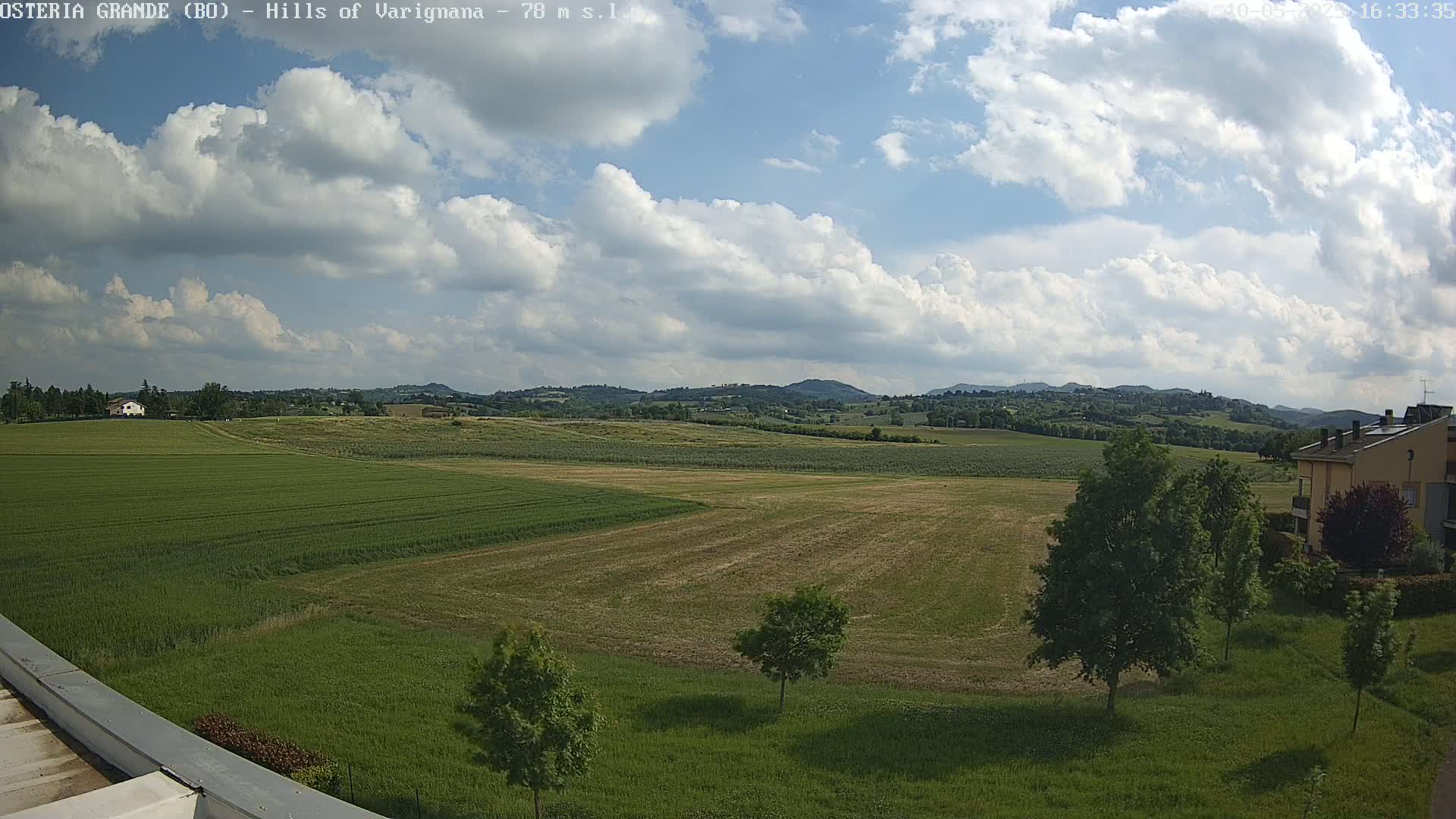 A partly cloudy day reveals rolling green hills and fields, with a few buildings visible in the distance.