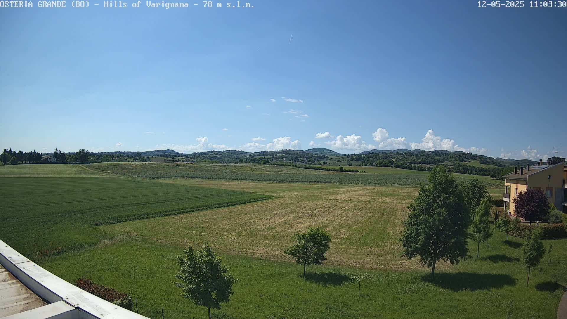 A sunny day reveals rolling green hills and fields, with a few scattered trees and a building visible in the distance.