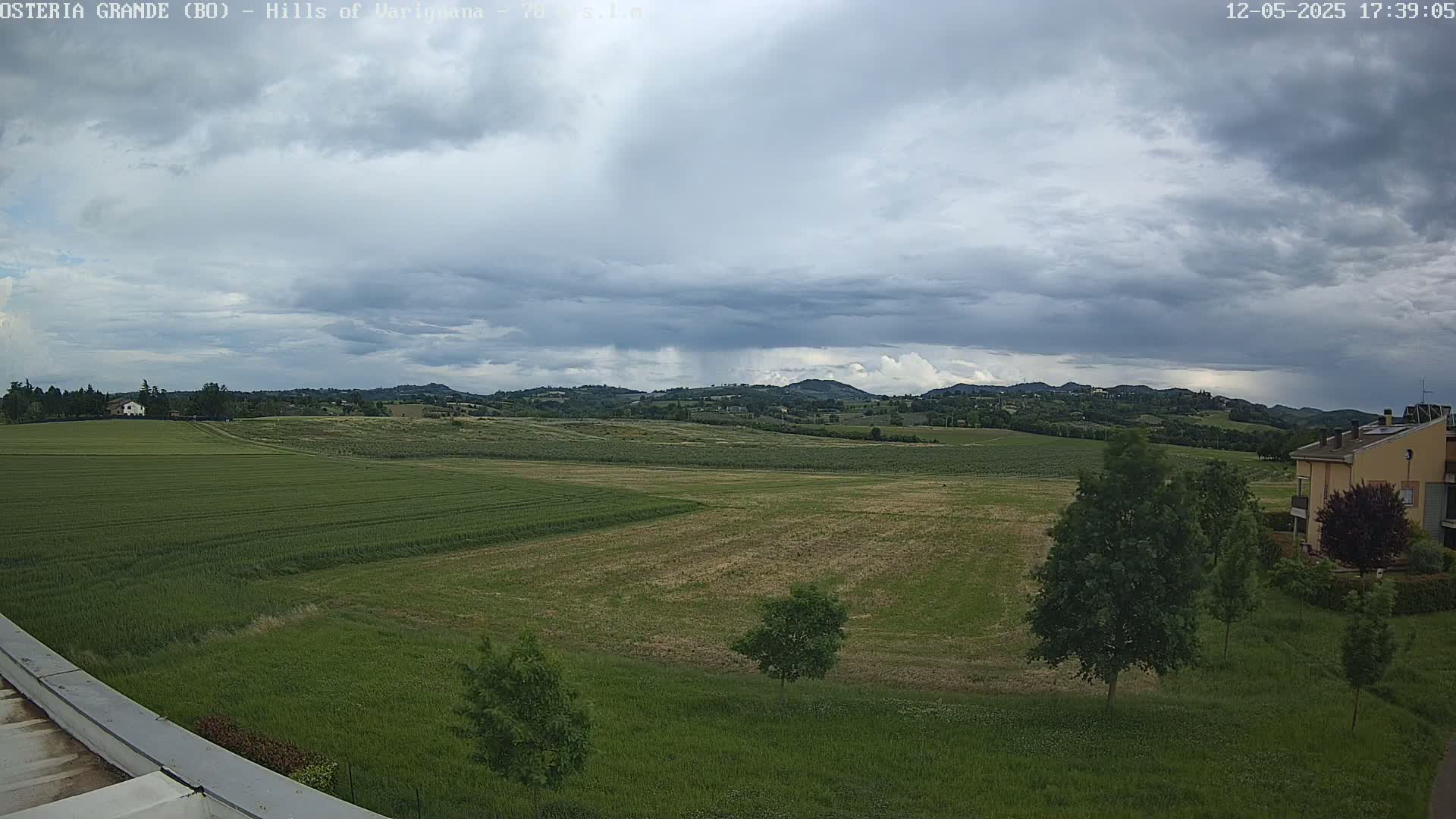 A sprawling, mostly green landscape of fields and low hills under a cloudy sky, with a few buildings visible in the distance.