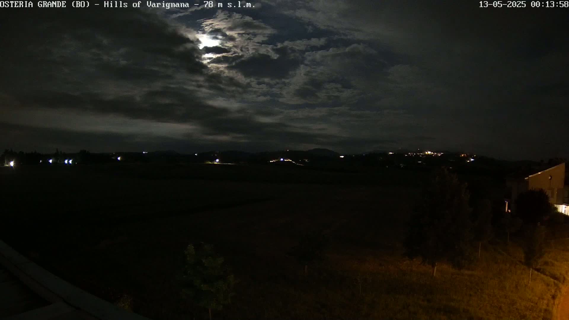 A nighttime view of dark, rolling hills under a partly cloudy sky illuminated by a bright moon.