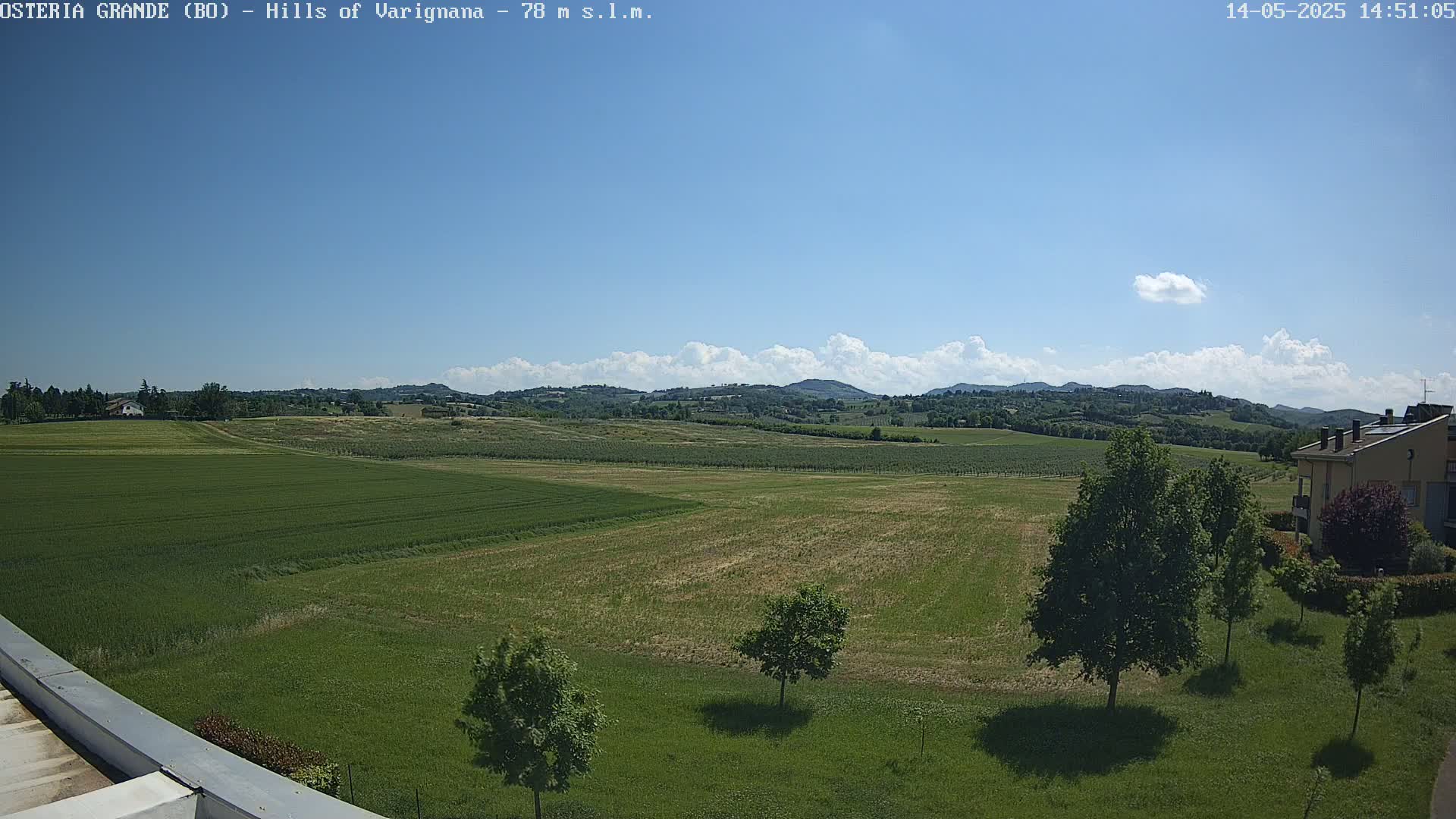 A sunny day reveals rolling green hills and fields under a mostly clear blue sky with a few scattered clouds.
