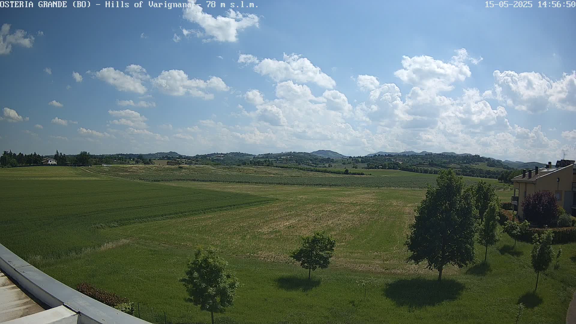 A partly cloudy sky overlooks a vast expanse of green fields and distant rolling hills.