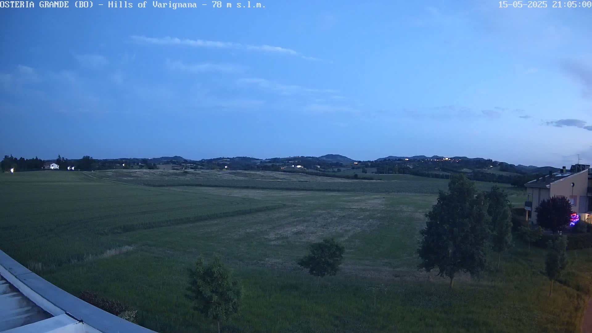 A twilight view shows a flat expanse of green farmland extending to rolling hills in the distance under a clear, dark blue sky.