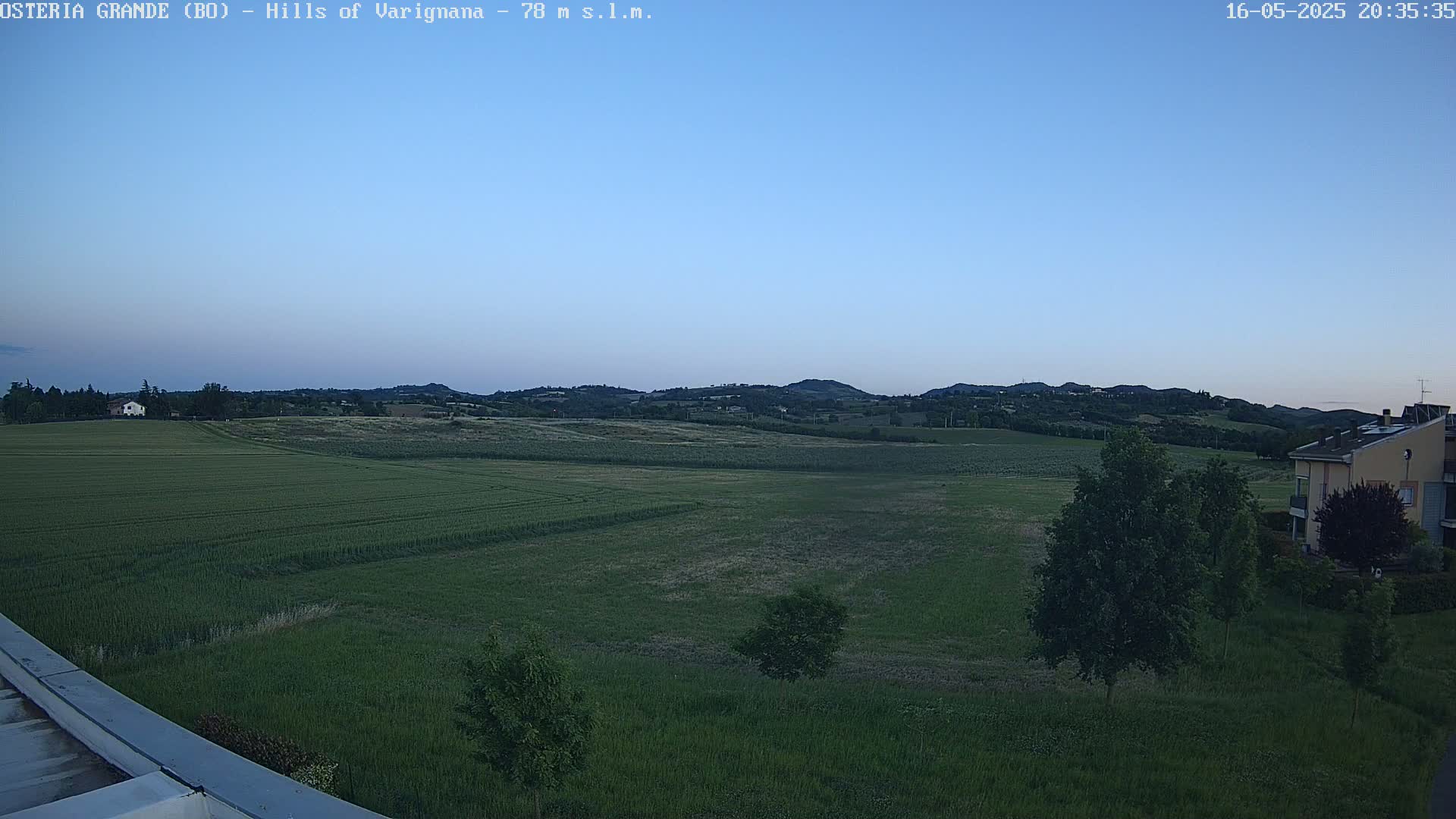 A wide, flat expanse of green fields stretches towards rolling hills under a clear, twilight sky.