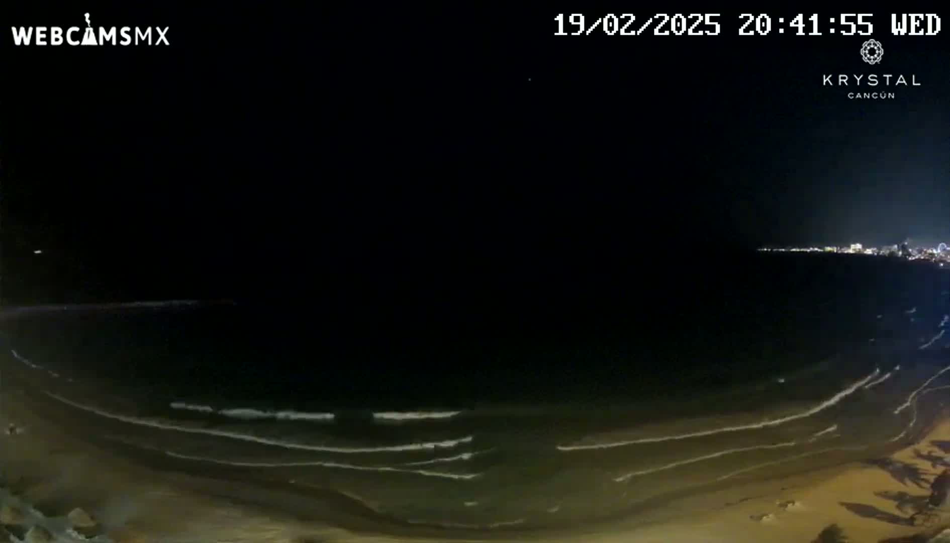A nighttime view of a beach with gently rolling waves under a clear, dark sky.