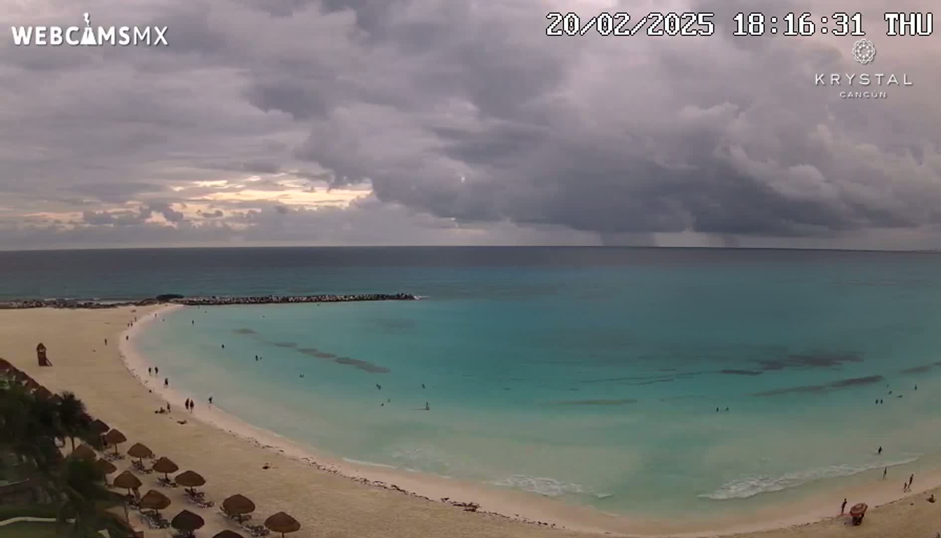 A sandy beach with turquoise water and a few people is visible under a mostly cloudy sky.