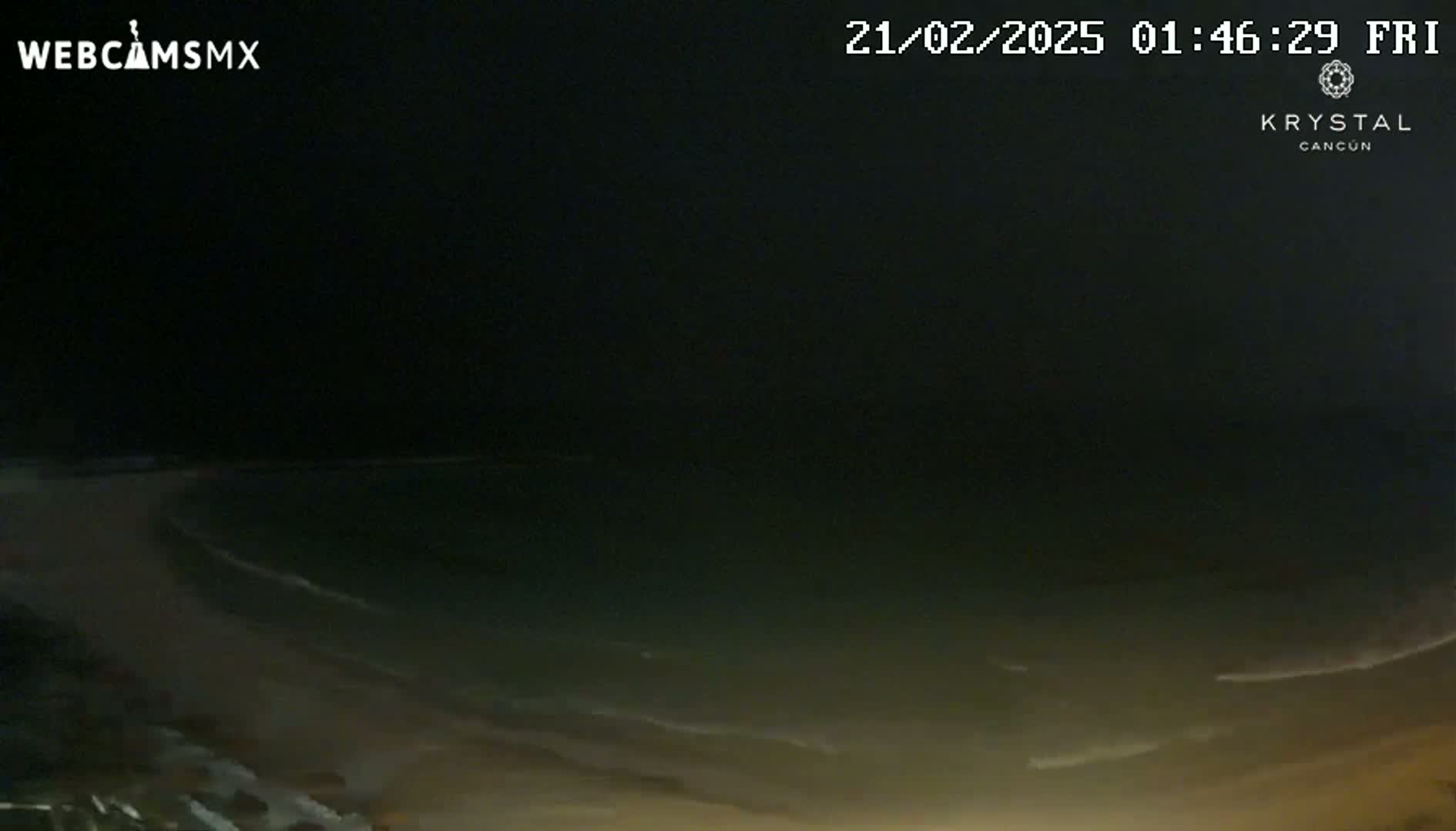 A dark nighttime beach scene shows gently lapping waves on a sandy shore under a clear, starless sky.