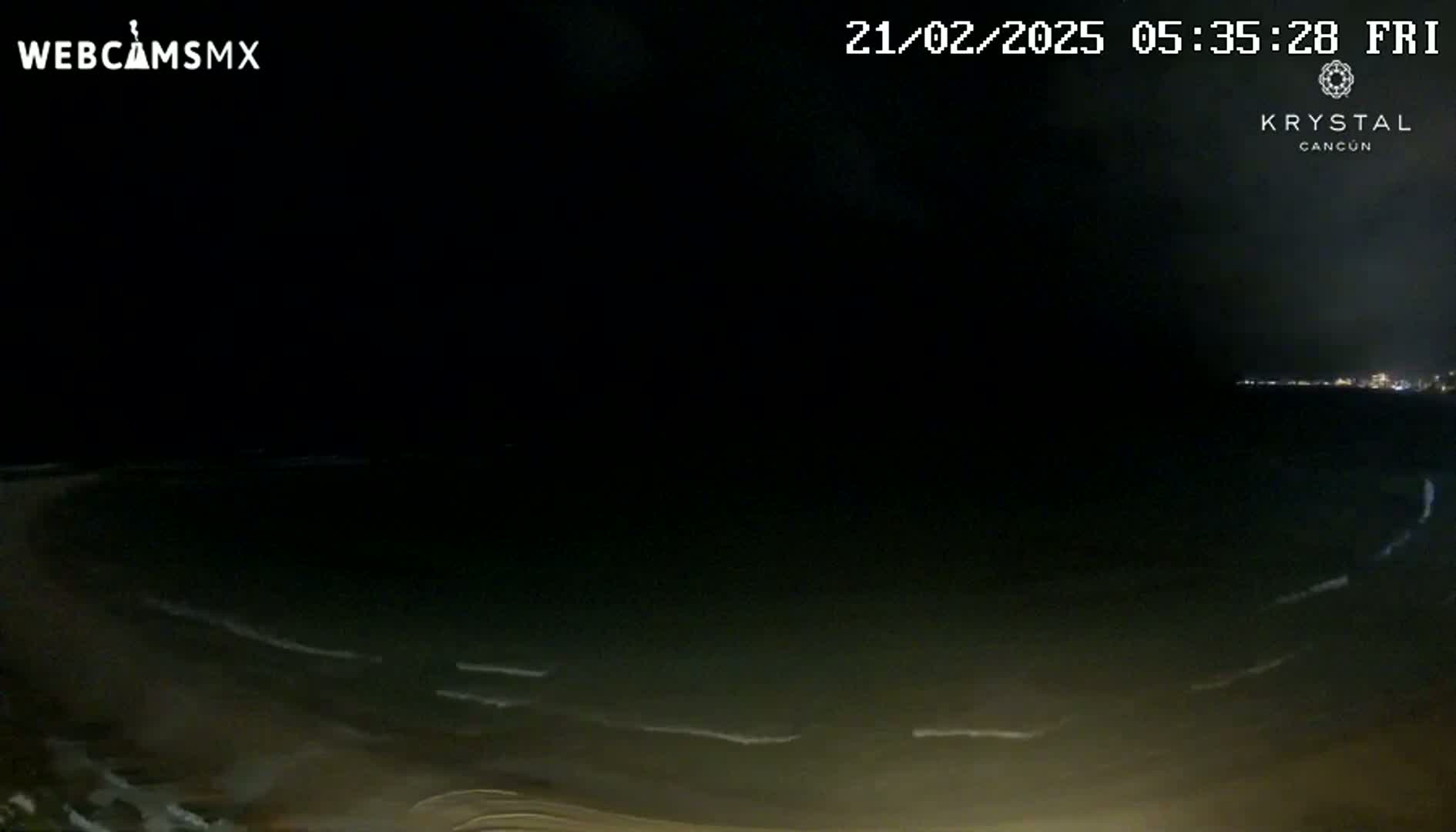 A dark, nighttime beach scene shows gentle waves lapping the shore under a mostly clear sky.