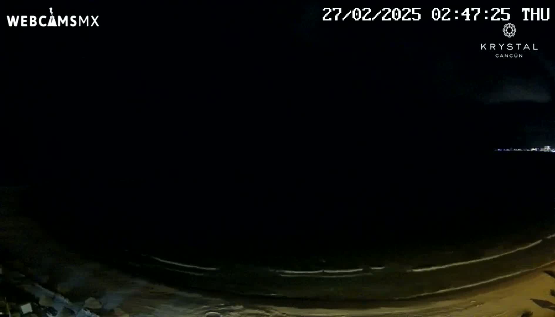 A dark nighttime beach scene shows a calm ocean with small waves lapping the shore.