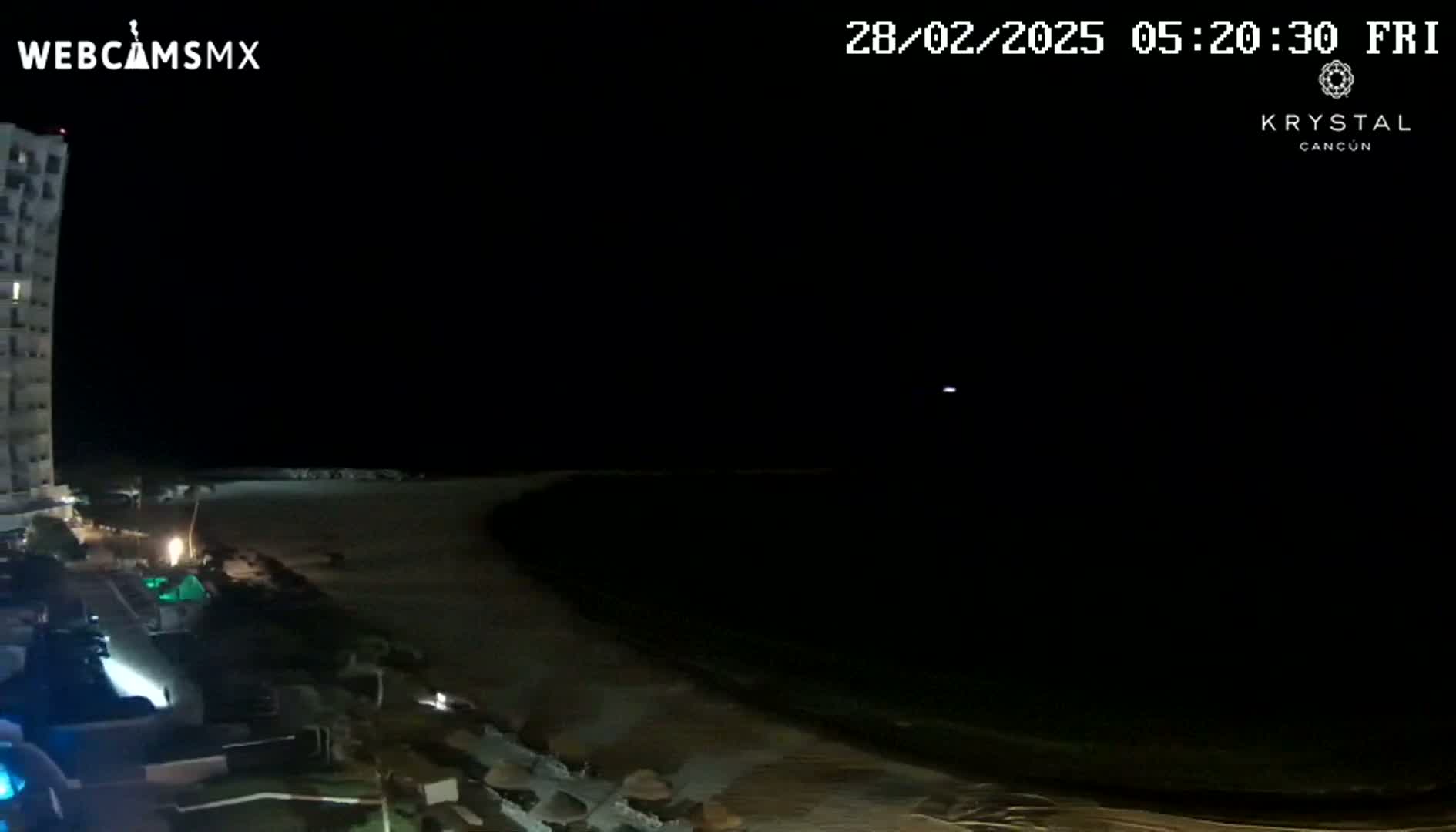 A nighttime view of a dark ocean shoreline next to a tall building under a clear, dark sky.