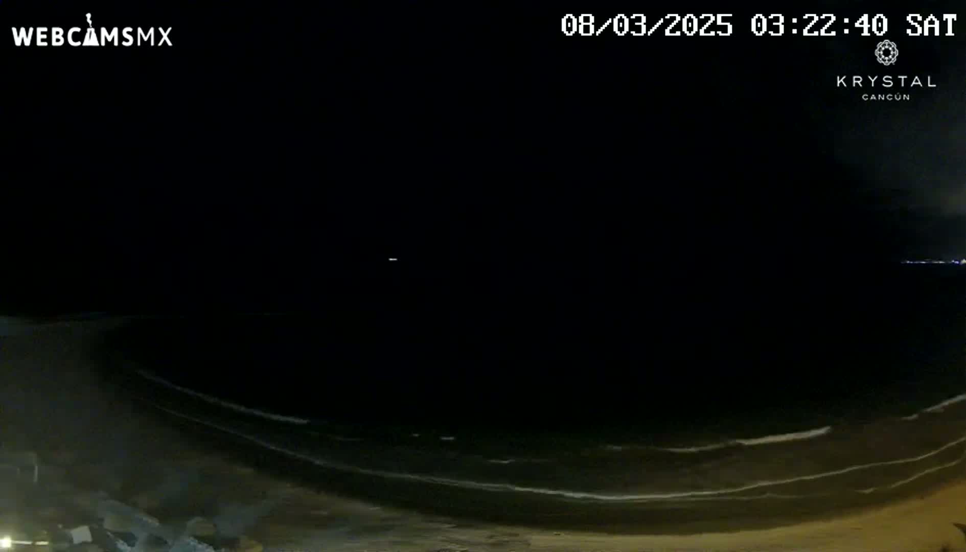A nighttime beach scene shows dark sand and gently lapping waves under a clear, dark sky.
