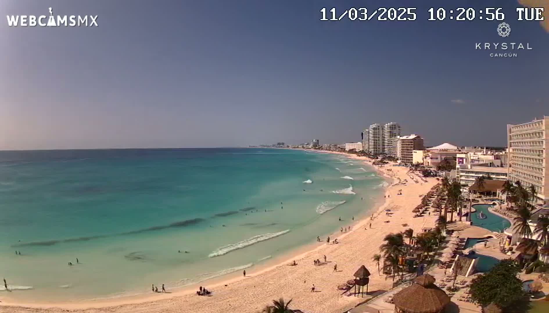 A sunny day at a beach with turquoise water, white sand, and several high-rise hotels along the shoreline.