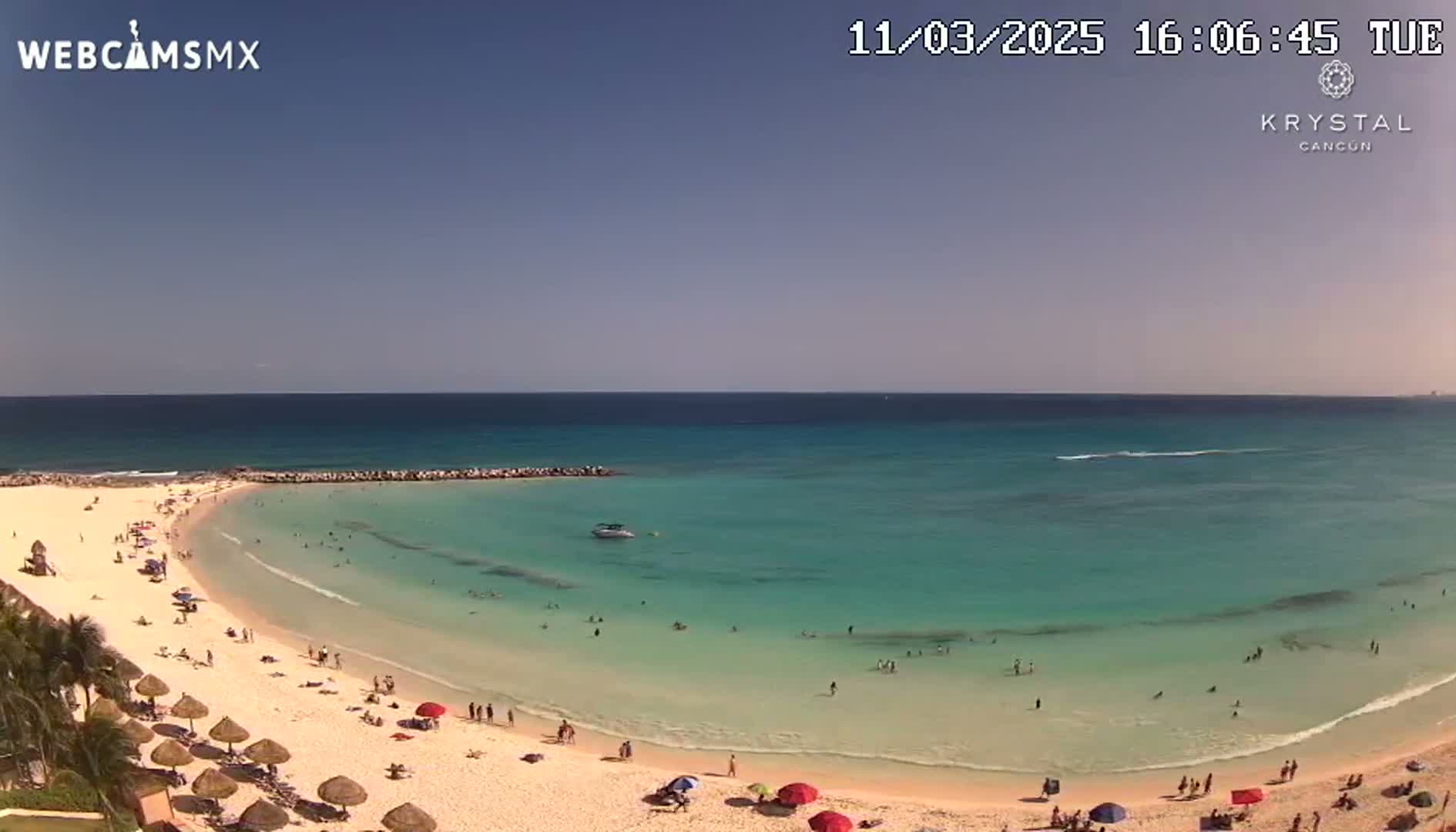 A sandy beach with calm, turquoise water and many people enjoying the sunny day.