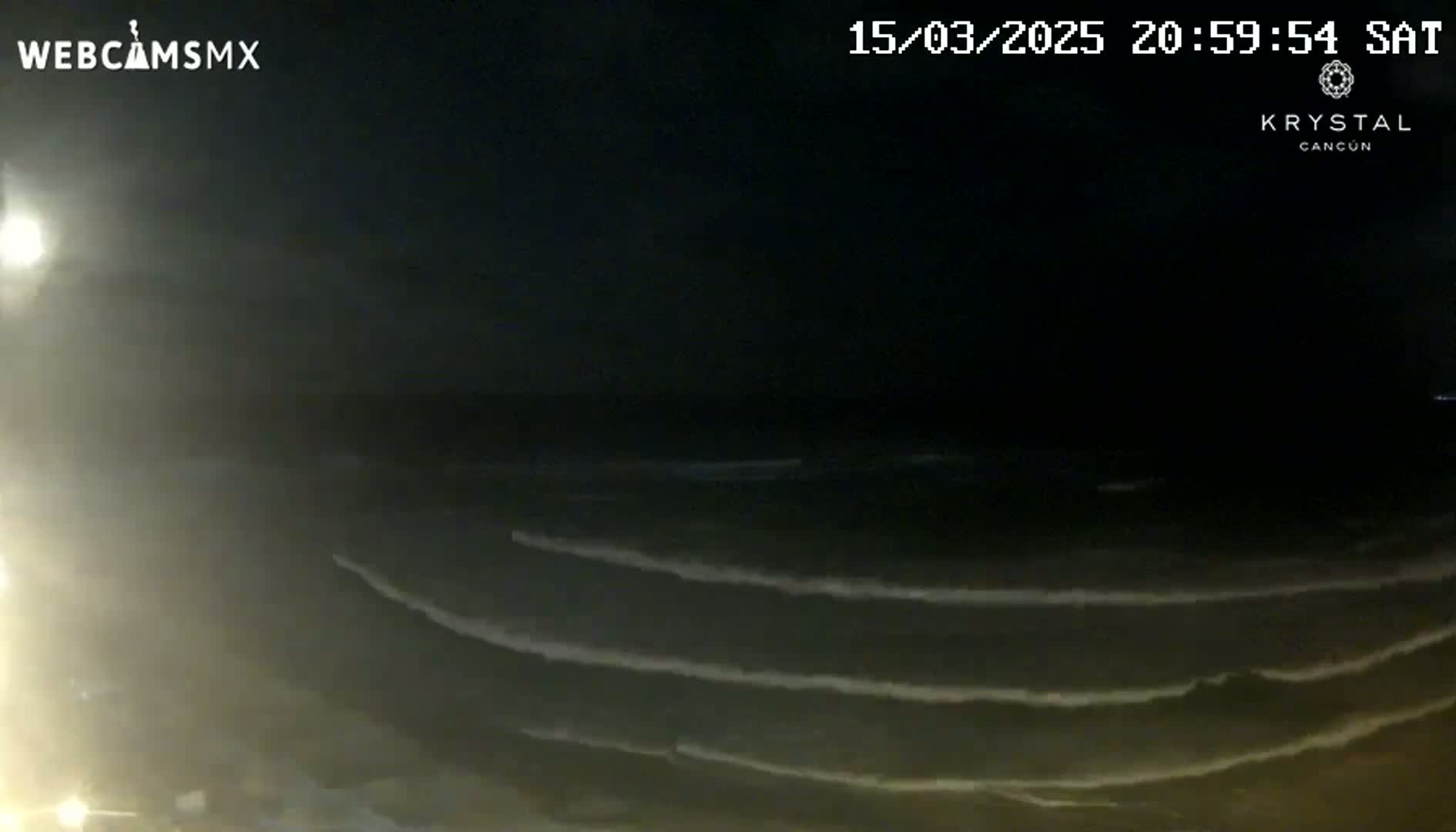 At night, several gentle waves roll onto a dark beach under a clear, dark sky.
