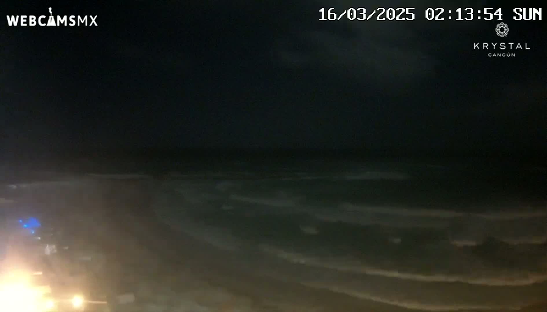 A nighttime view of dark ocean waves lapping a beach under a cloudy sky.