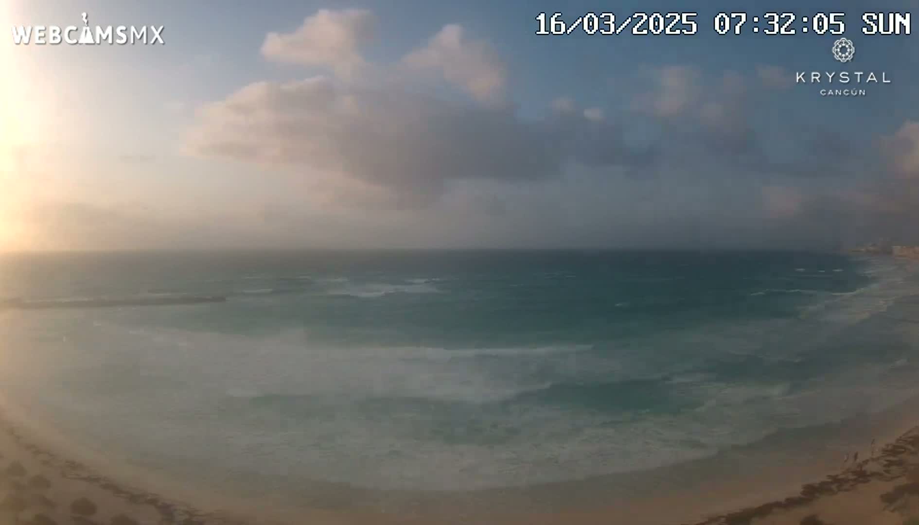 A partly cloudy sunrise over a beach with moderately sized waves.