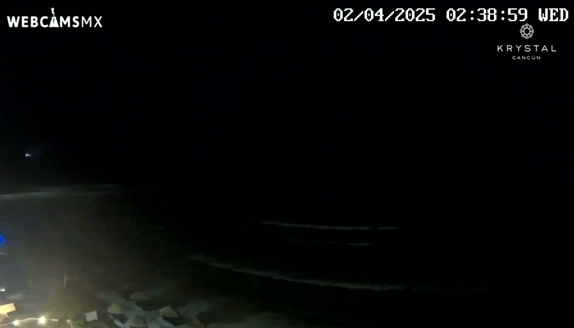 A dark nighttime beach scene shows gently lapping waves under a clear, starless sky.
