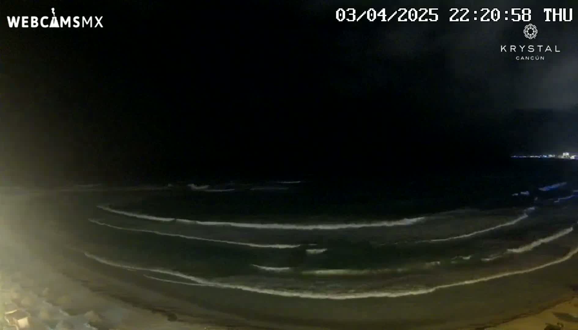 A nighttime view of gentle waves rolling onto a dark sandy beach under a mostly clear sky.