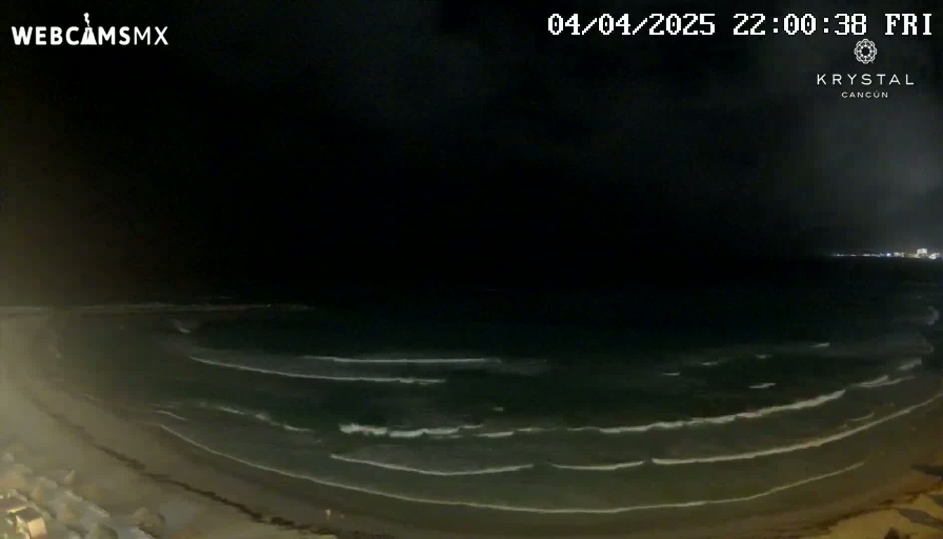 A nighttime beach scene shows gently rolling waves lapping a sandy shore under a dark sky.