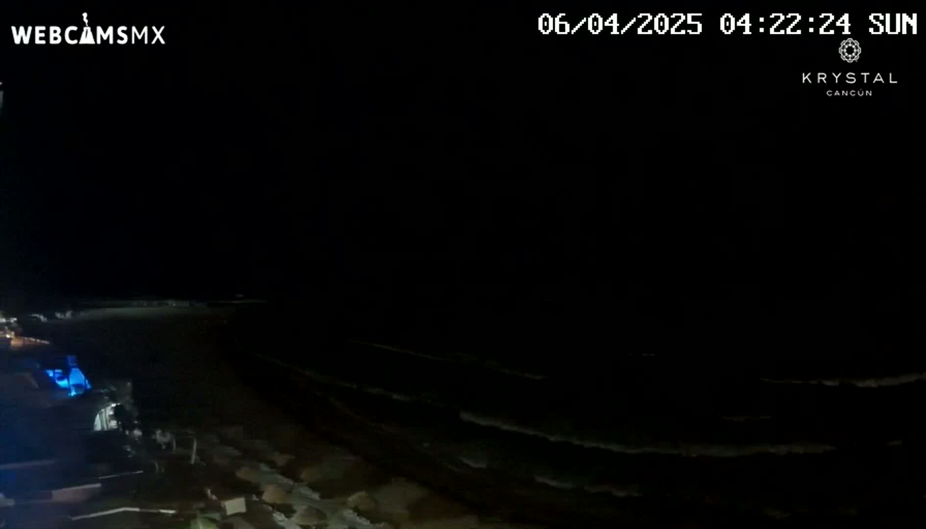 A nighttime view of a dark beach with gently lapping waves under a clear, starless sky.