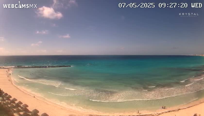 A mostly sunny day shows a beach with turquoise water lapping gently onto the shore.