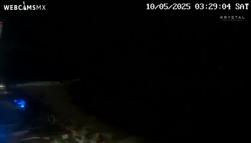 A nighttime, dark outdoor scene shows a small portion of a dimly lit area, possibly a parking lot or roadway, with a faint light source visible in the lower-left.