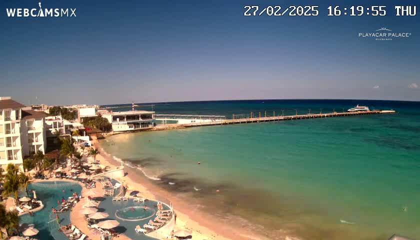 A beach resort with a long pier extending into clear turquoise water under a bright sunny sky.