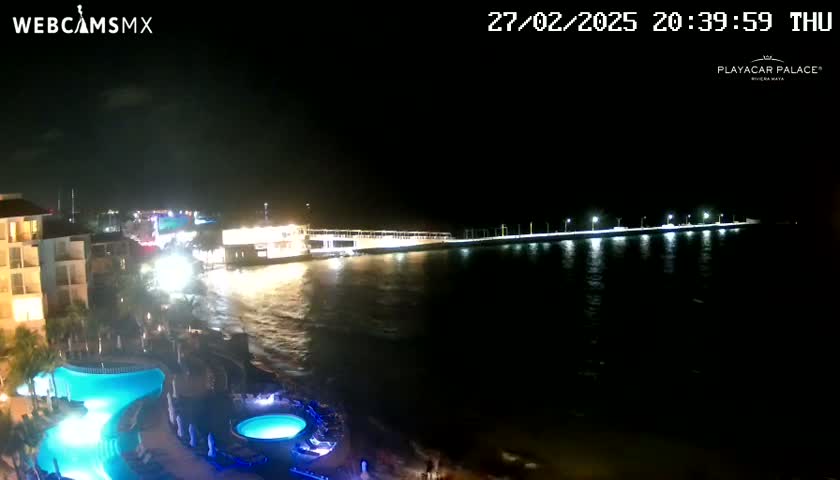 A nighttime view of a resort area with illuminated pools and a pier extending into dark water under a clear sky.