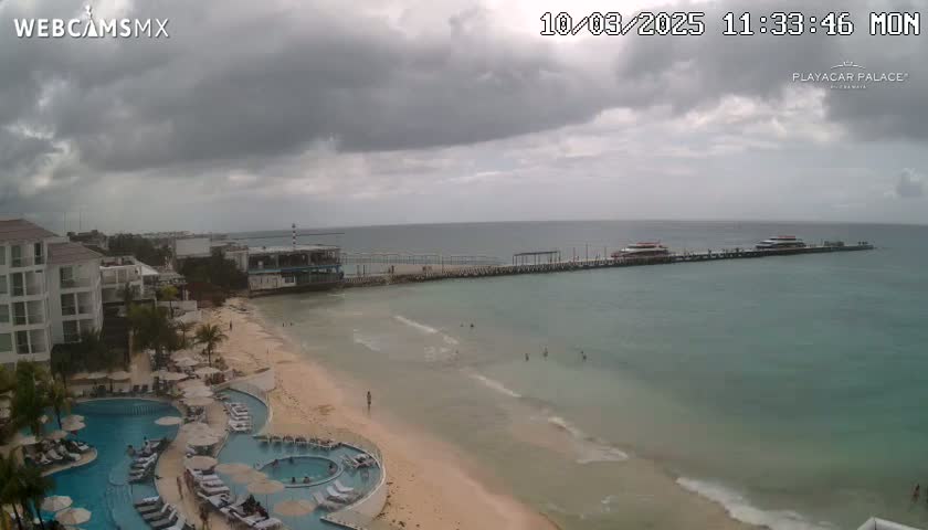 A beach with a resort, pool, and pier, under an overcast sky.