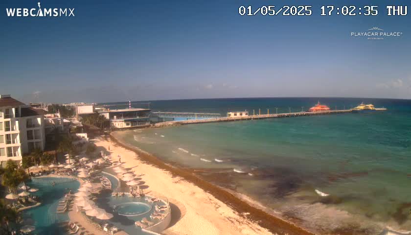 A beach resort with a long pier extending into clear turquoise water under a bright, sunny sky.