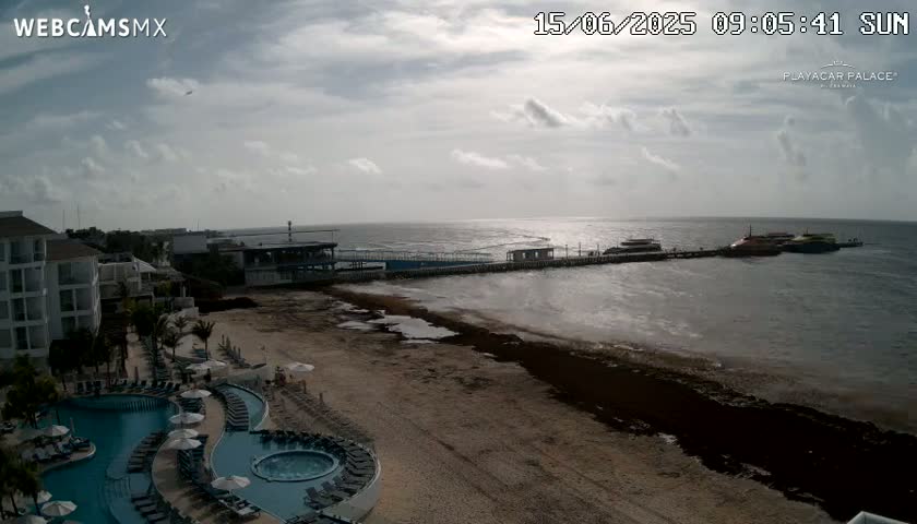 A beach with a resort, swimming pools, and a pier with boats is visible under a partly cloudy sky.