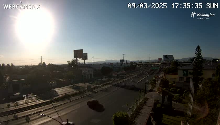 A sunny, mostly clear day overlooking a highway with several buildings and billboards visible in the distance.
