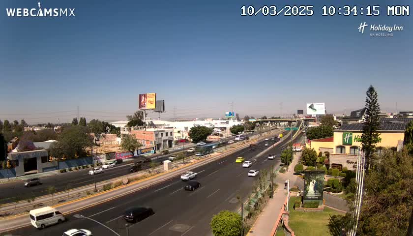 A sunny day reveals a highway scene with light traffic, buildings, and lush greenery, including a Holiday Inn.