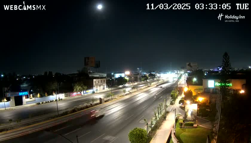 A brightly lit highway cuts through a city at night under a full moon, with a few vehicles visible.