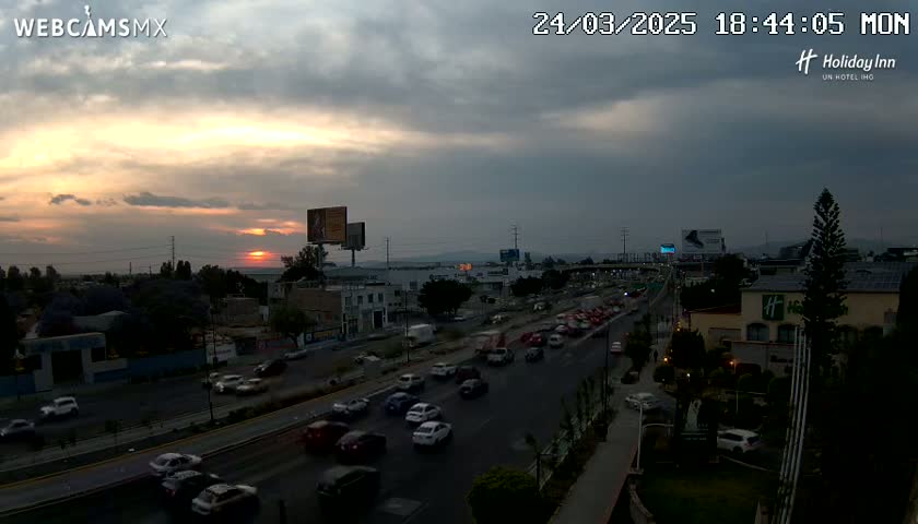 A highway with moderate traffic is seen at sunset under a partly cloudy sky.