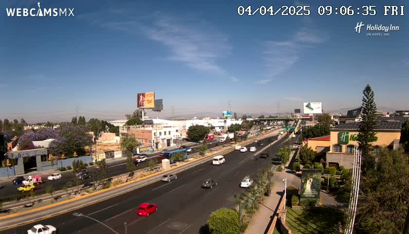 A highway with moderate traffic flows through a city under a clear, sunny sky.