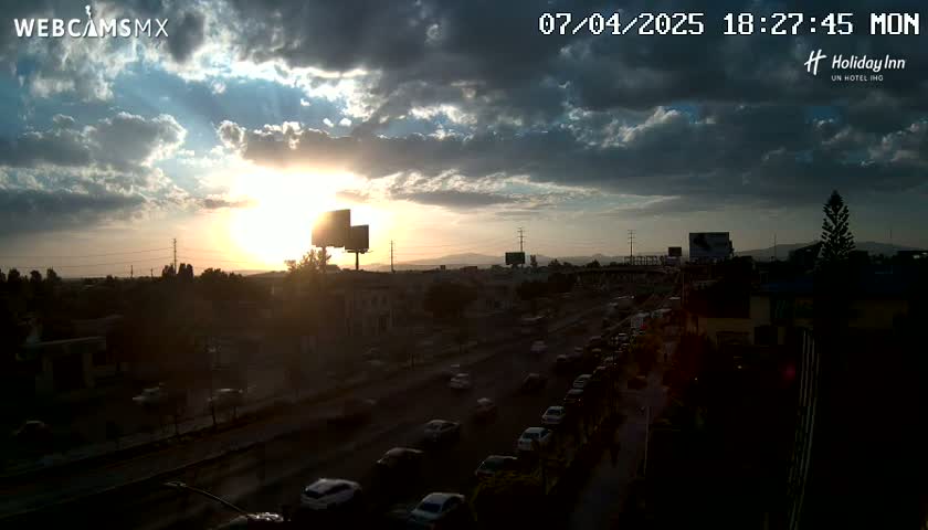 A partly cloudy sunset illuminates a highway with heavy traffic, as seen from an elevated vantage point.
