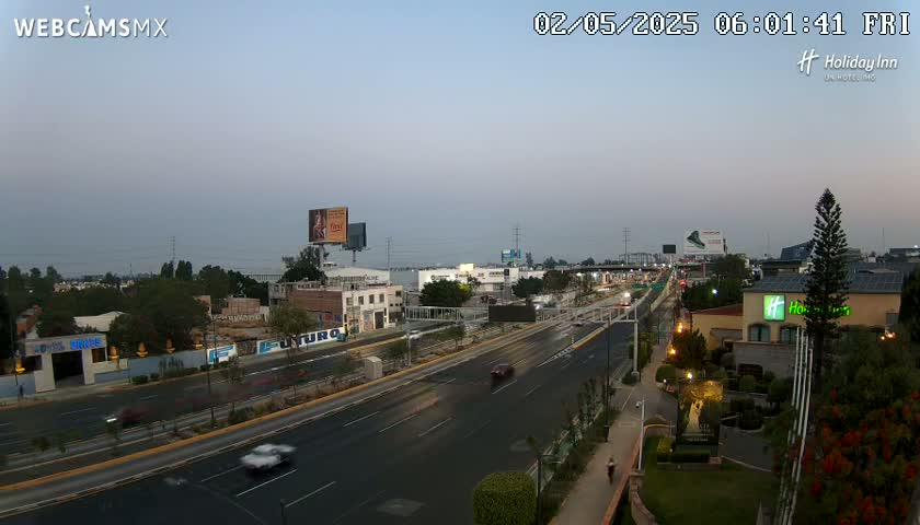 A wide shot of a multi-lane highway with light traffic under a dusky sky, showing buildings and vegetation alongside the road.